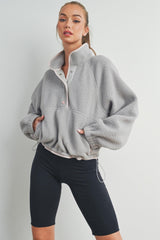 woman wearing a grey fleece pullover with a high collar and snap buttons, paired with black bike shorts