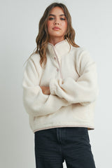 woman wearing a cream-colored fleece pullover with a snap collar and relaxed fit, standing with arms crossed