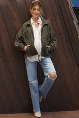 woman wearing a green maternity jacket over a white blouse and distressed jeans, showing her baby bump
