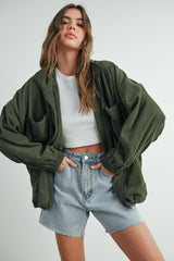 woman wearing an oversized olive green corduroy jacket over a white crop top and high-waisted denim shorts