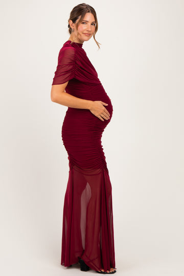 woman wearing a burgundy maternity gown with draped details and a visible baby bump