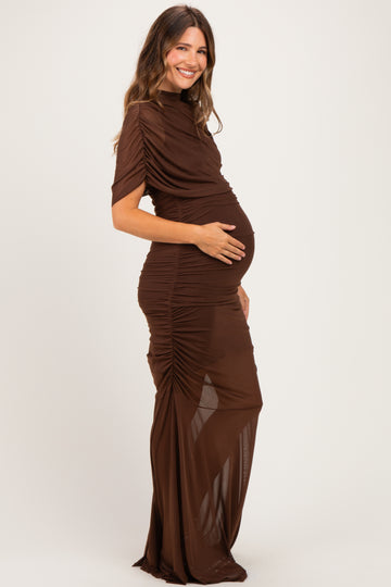 woman wearing a brown ruched maternity dress with short sleeves and a slit, gently holding her baby bump