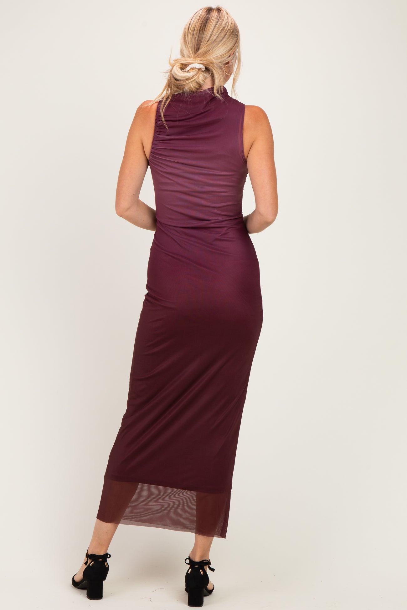 woman wearing a back view of a burgundy sleeveless maxi dress with a fitted silhouette and sheer hem