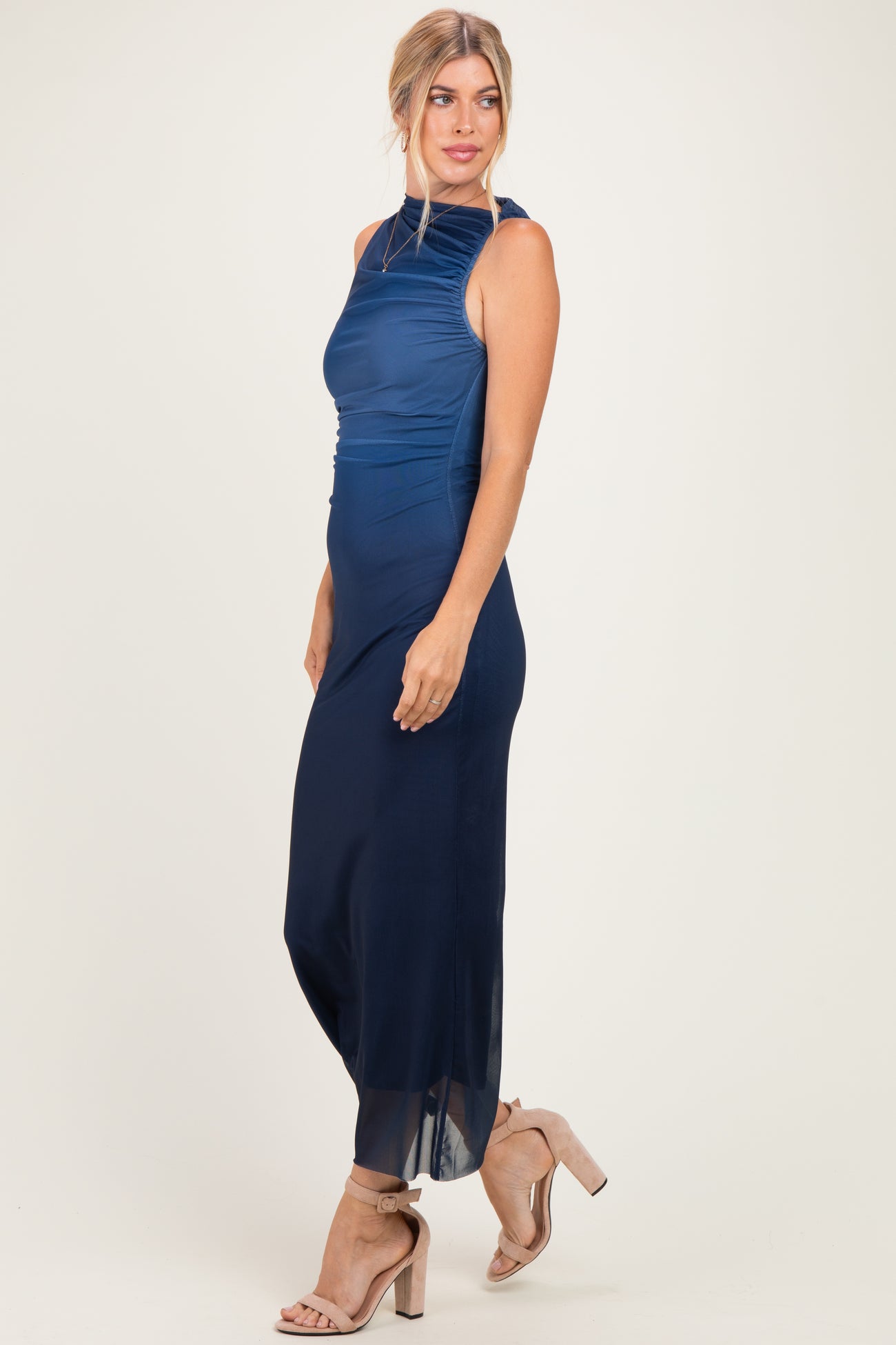 woman wearing a navy blue sleeveless maxi dress with a ruched bodice and sheer hem, paired with strappy heels