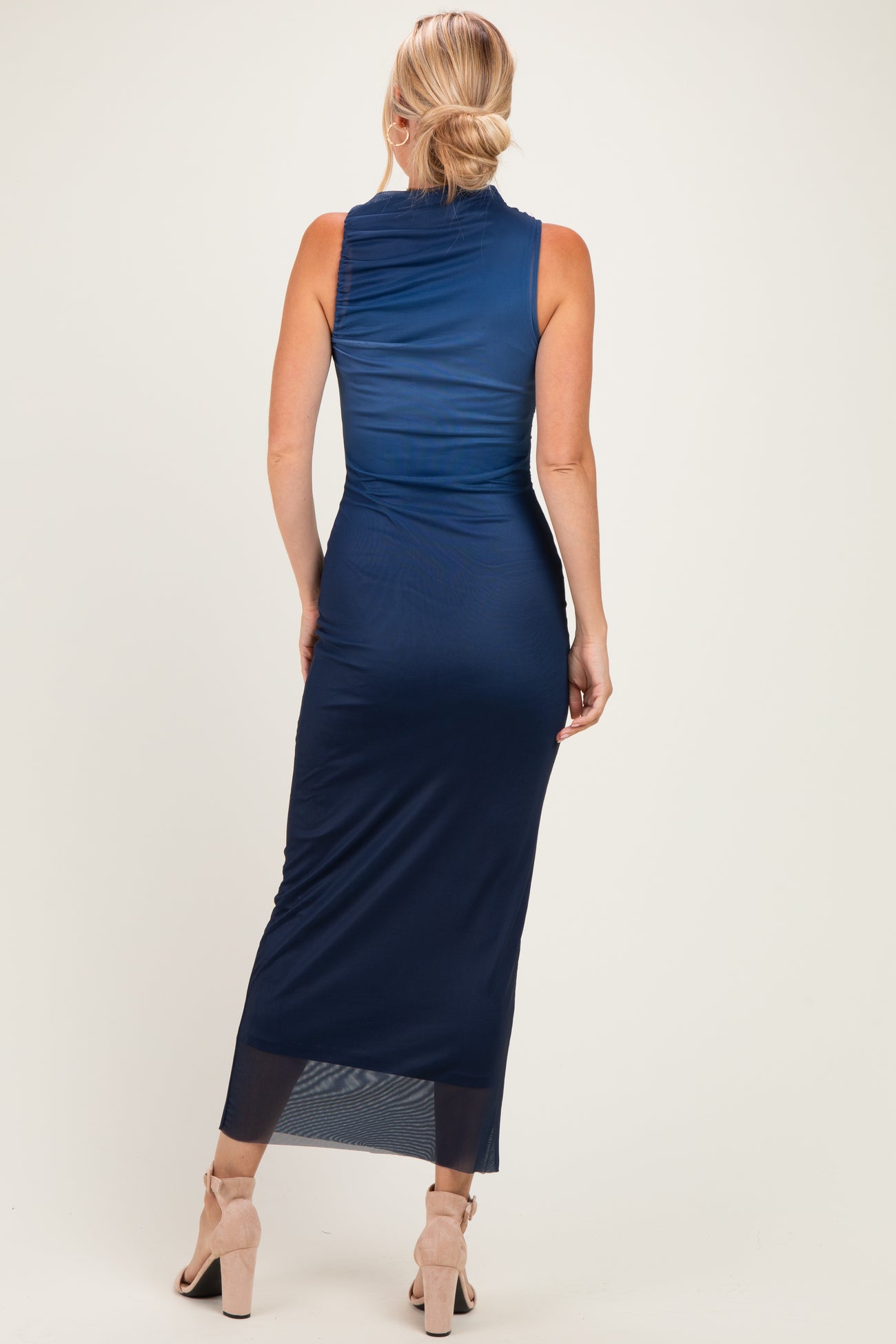 woman wearing a navy blue sleeveless maxi dress with a fitted silhouette and sheer bottom hem, shown from the back