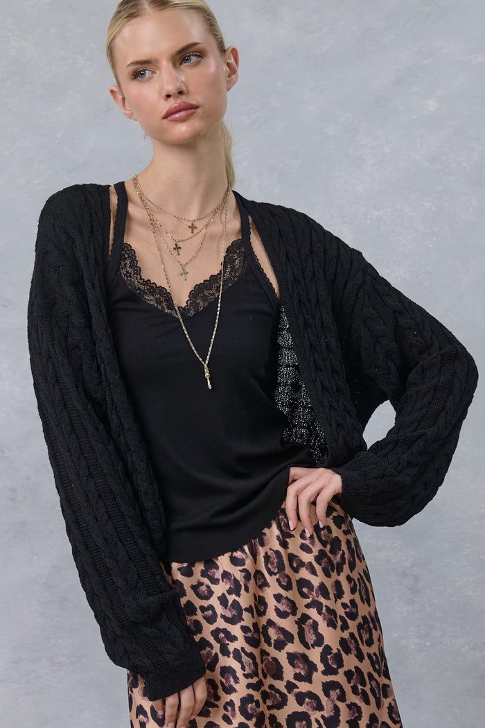 woman wearing a black cable knit cardigan over a black lace camisole and pink leopard print skirt