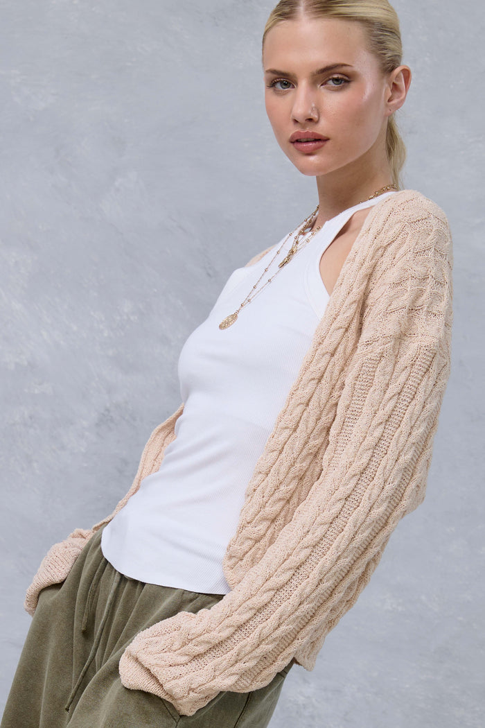 woman wearing a light beige cable-knit cardigan over a white tank top and olive green joggers, styled with a necklace