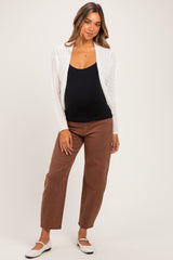 woman wearing a black maternity tank top and white cable knit cardigan with brown maternity jeans, showing baby bump