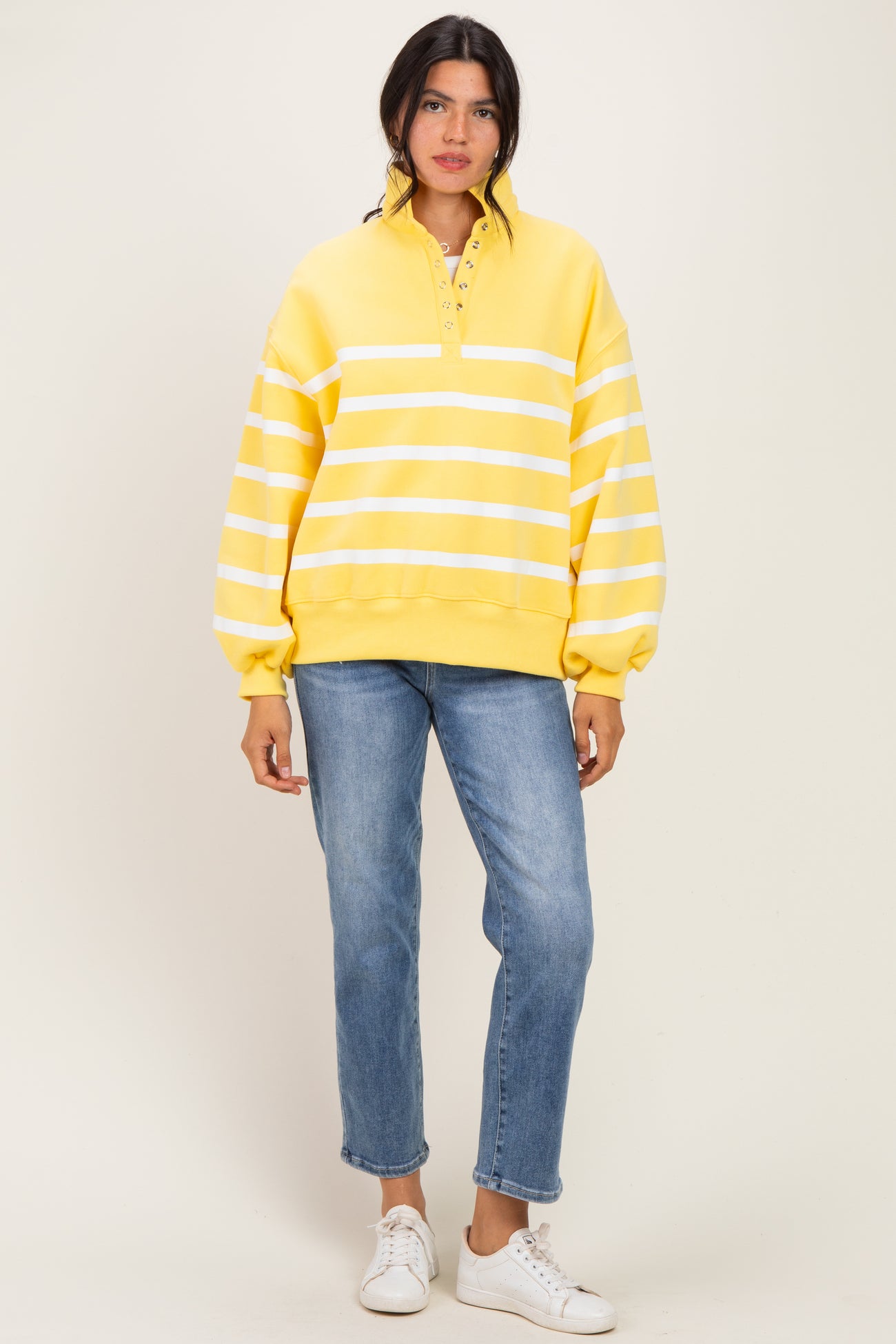 woman wearing a yellow striped pullover sweatshirt with a high collar and front buttons, paired with light blue jeans and sneakers