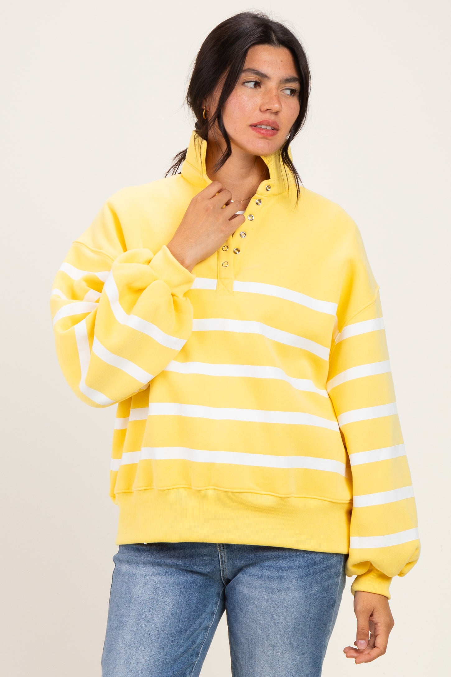 woman wearing a yellow striped oversized sweatshirt with a collar and button details, paired with blue jeans