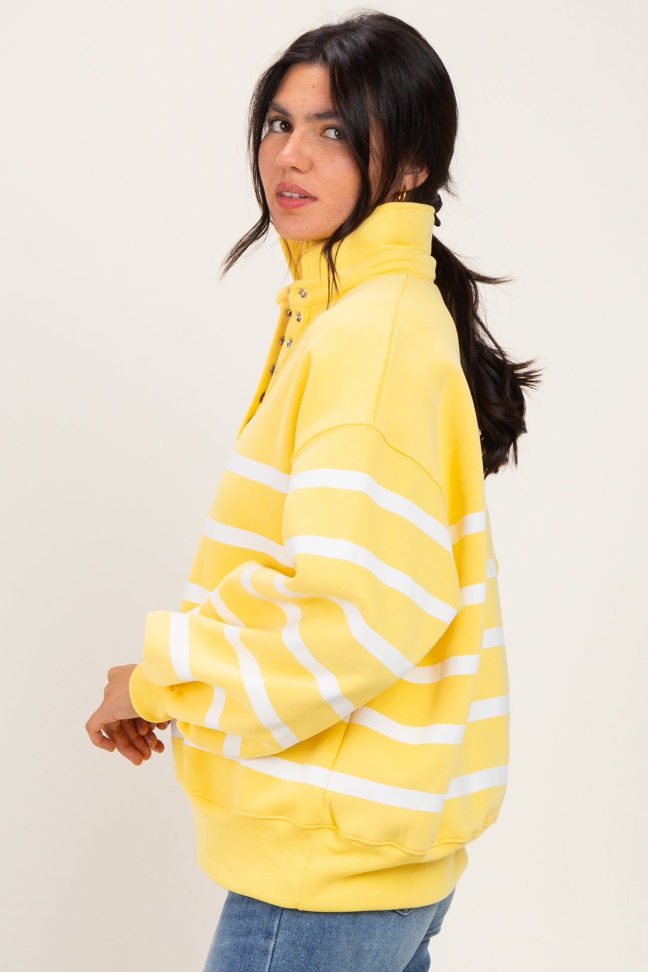 woman wearing a yellow and white striped oversized sweatshirt with a high collar and button detail