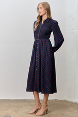 woman wearing a navy blue long sleeve midi dress with red polka dots and a smocked bodice