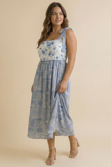 woman wearing a blue floral print midi dress with adjustable straps and a fitted bodice