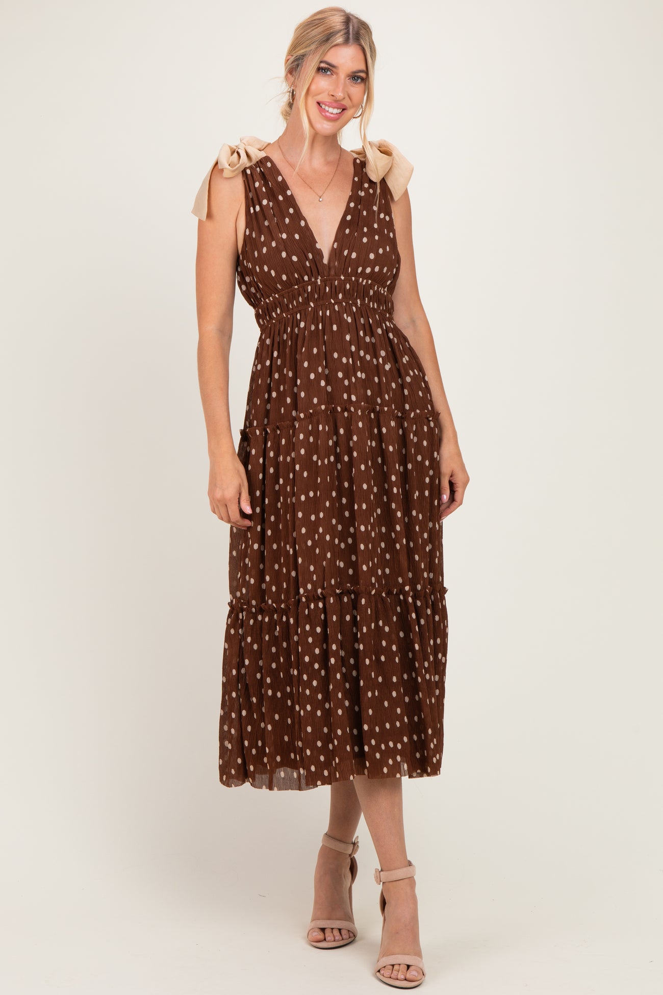 woman wearing a brown polka dot maxi dress with tie straps and a tiered skirt, styled with beige heels