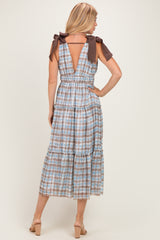 woman wearing a beige and blue checkered midi dress with tied shoulder straps and a tiered skirt, shown from the back