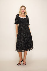 woman wearing a black floral midi dress with short puff sleeves and a square neckline, standing against a neutral background