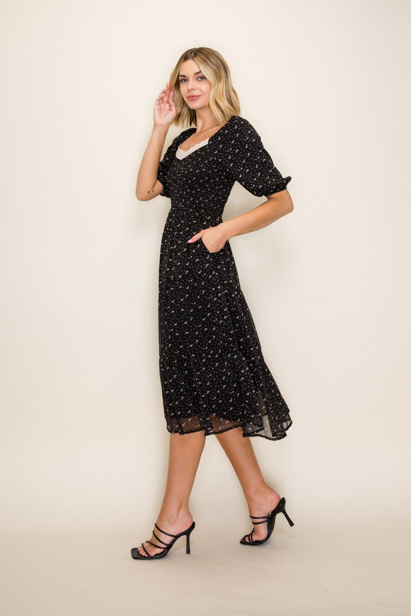 woman wearing a black floral midi dress with short puff sleeves and pockets, styled with high-heeled sandals