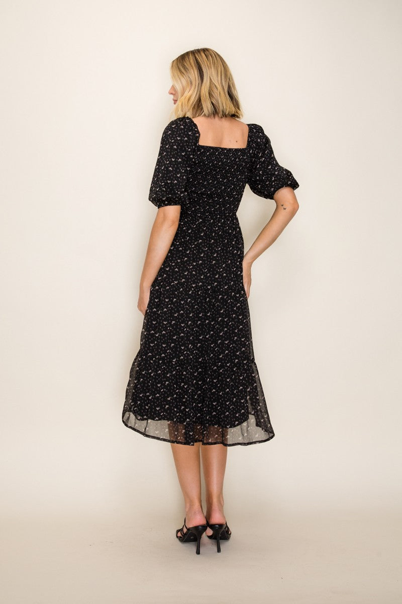 woman wearing a black floral midi dress with puff sleeves, showing a square back and flowing skirt