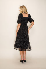 woman wearing a black floral midi dress with puff sleeves, showing a square back and flowing skirt
