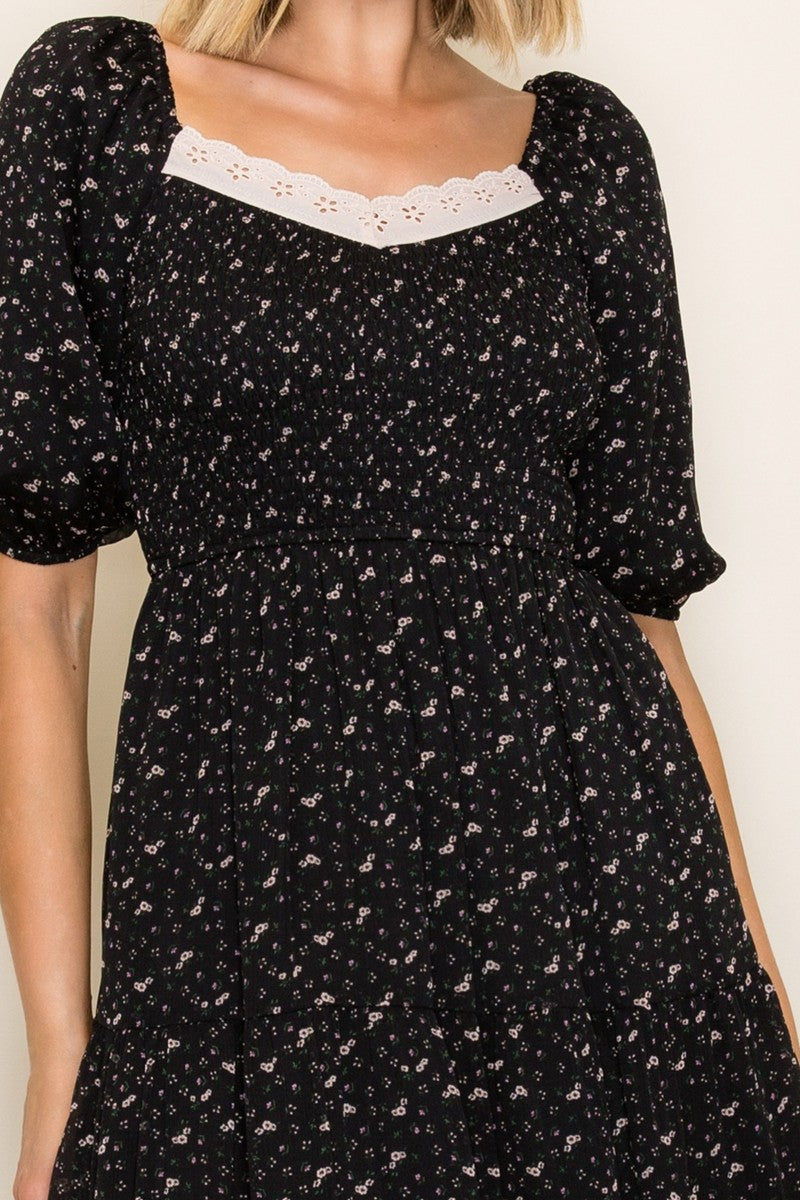 woman wearing a black floral print midi dress with puff sleeves and a lace-trimmed neckline