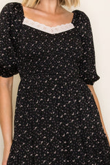 woman wearing a black floral print midi dress with puff sleeves and a lace-trimmed neckline