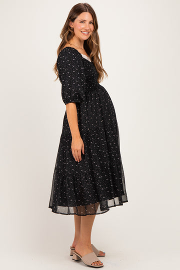 woman wearing a black floral maternity dress with short puff sleeves and a tiered skirt, showing her baby bump