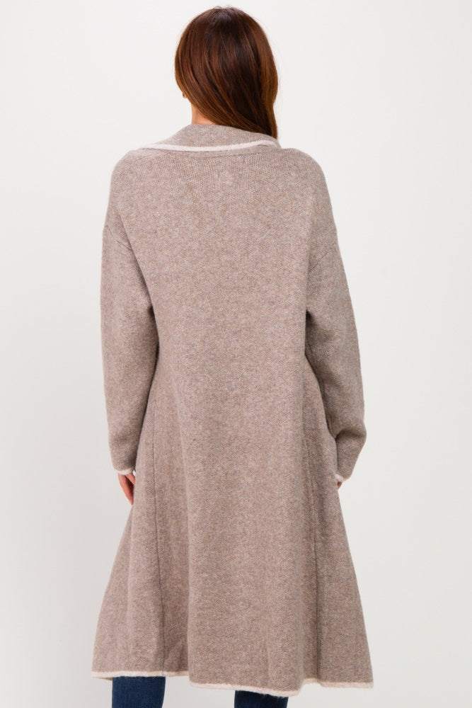 woman wearing a long beige cardigan with a cinched waist and a flared bottom, shown from the back