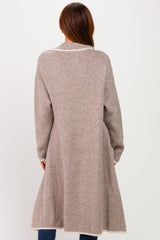 woman wearing a long beige cardigan with a cinched waist and a flared bottom, shown from the back