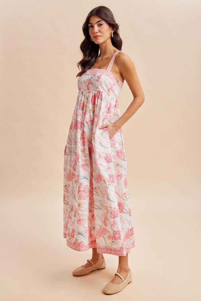 woman wearing a floral midi dress with pink and white hues and pockets, styled with woven flats
