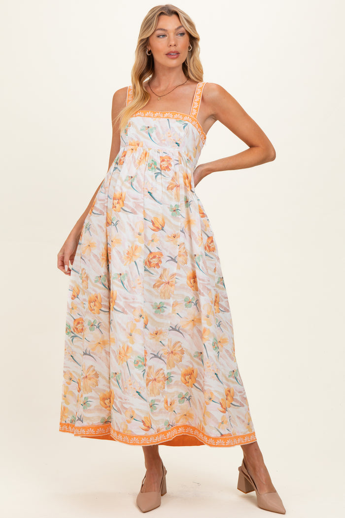 woman wearing a floral maternity maxi dress in orange and yellow with spaghetti straps and a flowing silhouette