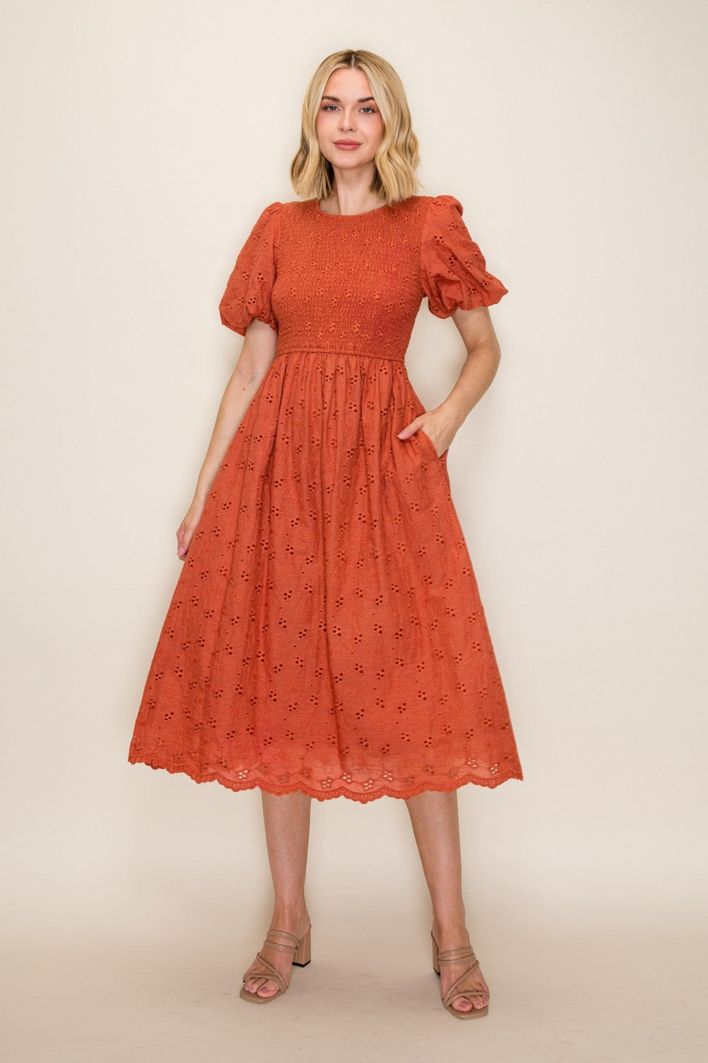 woman wearing an orange smocked midi dress with puff sleeves and pockets