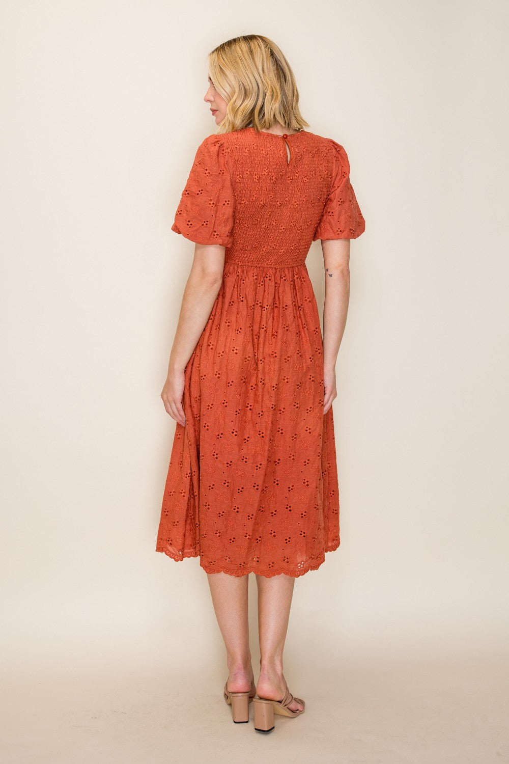 woman wearing an orange midi dress with short puff sleeves and floral embroidery, showing the back view
