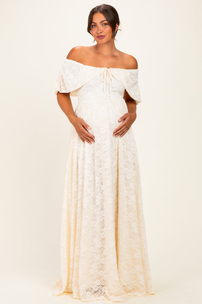 woman wearing a cream off-the-shoulder lace maternity maxi dress and cradling her baby bump
