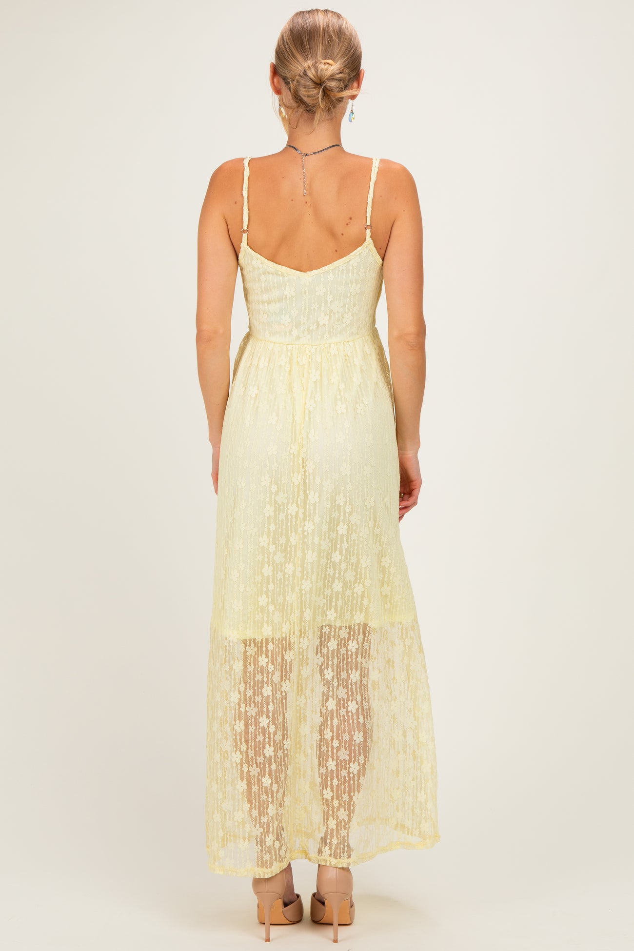 woman wearing a light yellow lace maxi dress with a fitted bodice and a flowing skirt, shown from the back