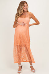 woman wearing a peach maternity maxi dress with a sheer overlay and holding her baby bump