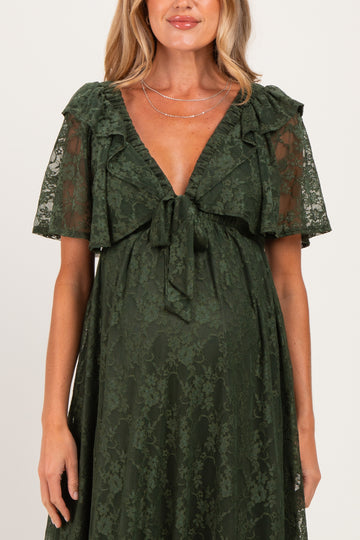 woman wearing a dark green lace maternity dress with short flutter sleeves and a tie detail at the chest, baby bump visible