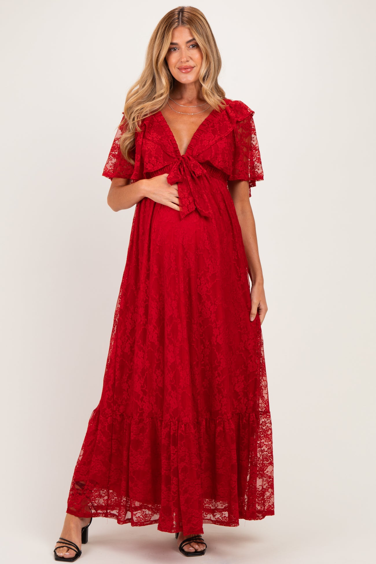 woman wearing a red lace maternity dress with short sleeves and a tie at the waist, showcasing her baby bump