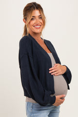 woman wearing a navy blue cardigan over a gray top, cradling her baby bump while smiling