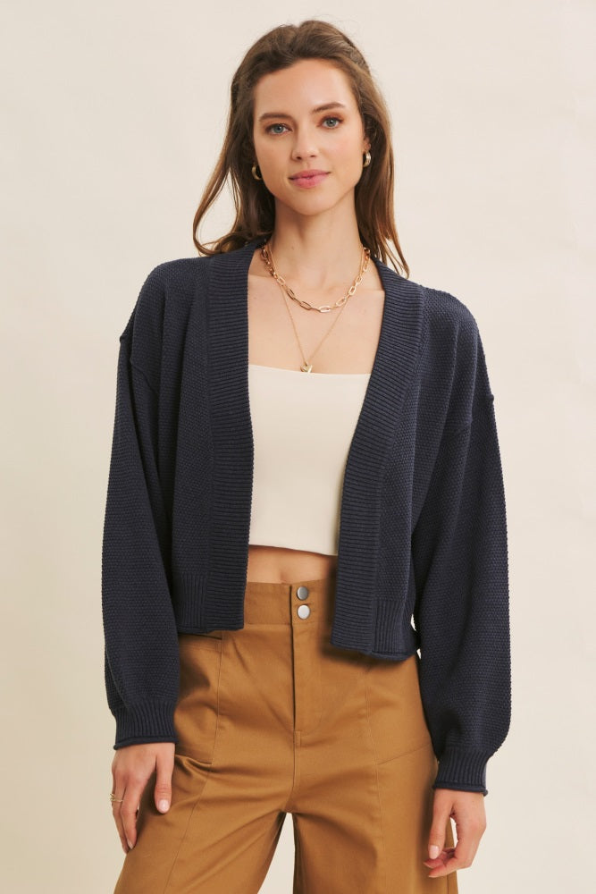 woman wearing a navy blue cropped cardigan over a beige top and styled with brown high-waisted trousers