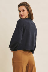 woman wearing a navy cropped sweater with long sleeves and a relaxed fit, paired with tan high-waisted trousers