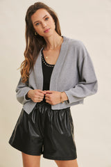 woman wearing a gray cropped cardigan over a black tank top and black faux leather shorts