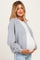 woman wearing a light gray oversized cardigan over a white top, holding her baby bump in a maternity wear style
