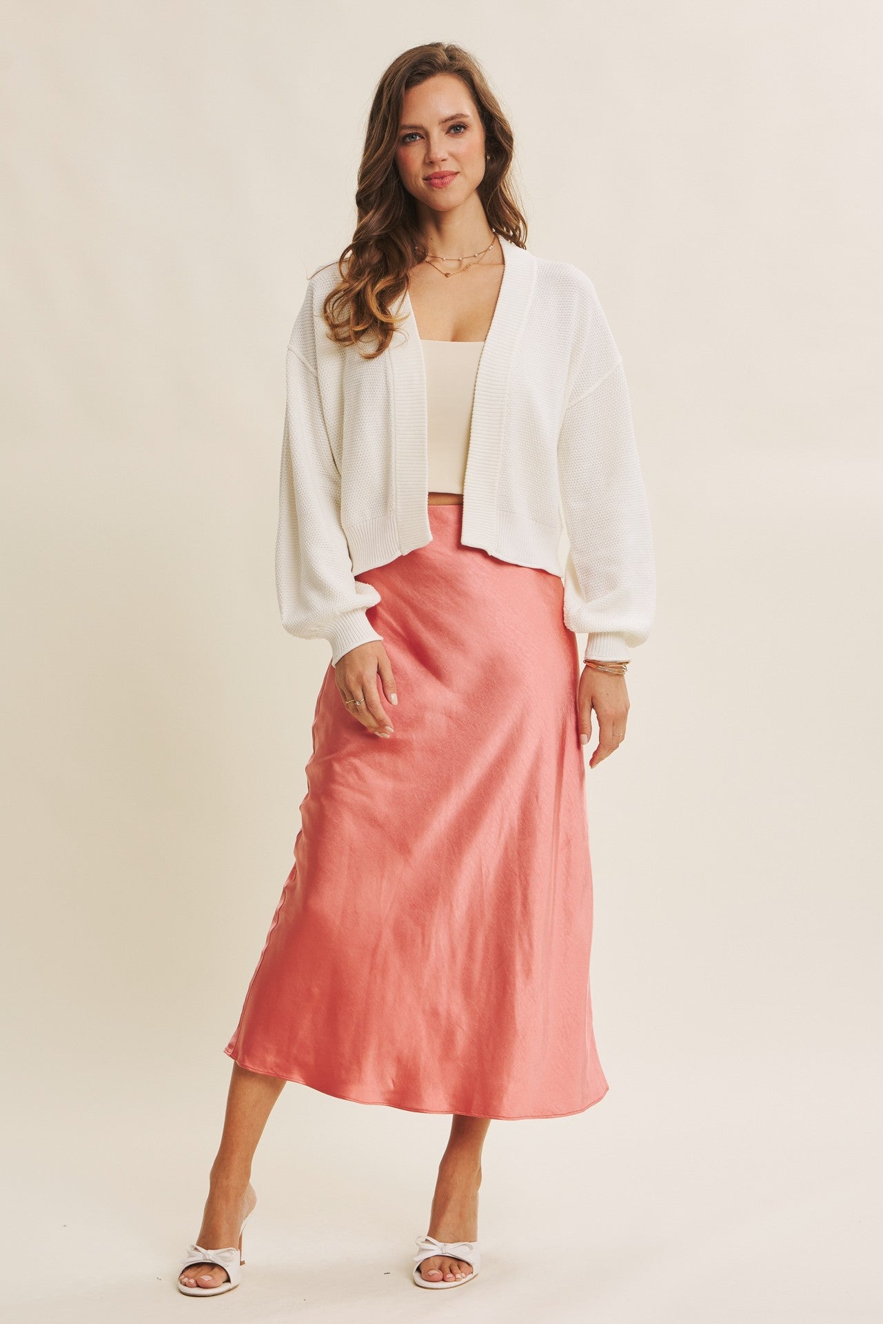 woman wearing a white cropped cardigan and a pink satin midi skirt with a slight sheen