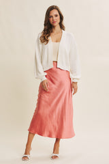 woman wearing a white cropped cardigan and a pink satin midi skirt with a slight sheen