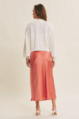 woman wearing a white textured cropped sweater and a flowing coral midi skirt from the back