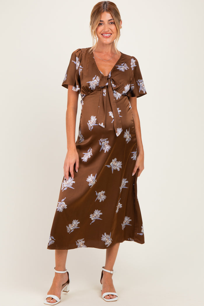 woman wearing a brown floral maternity dress with a tie front and short sleeves, showcasing her baby bump