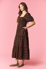 woman wearing a brown polka dot maxi dress with puff sleeves and smocked bodice, styled with side pockets