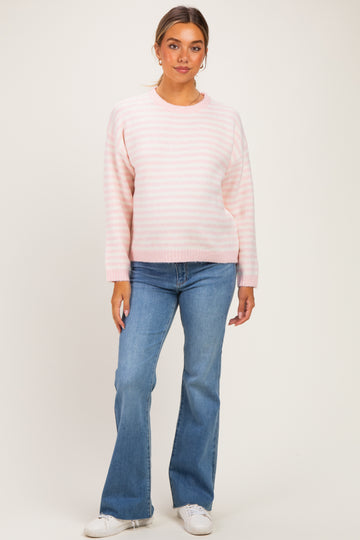 woman wearing a light pink striped maternity sweater and blue flared jeans, with a relaxed fit