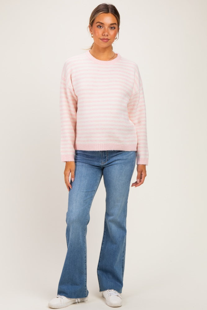 woman wearing a light pink striped maternity sweater and blue flared jeans, with a relaxed fit