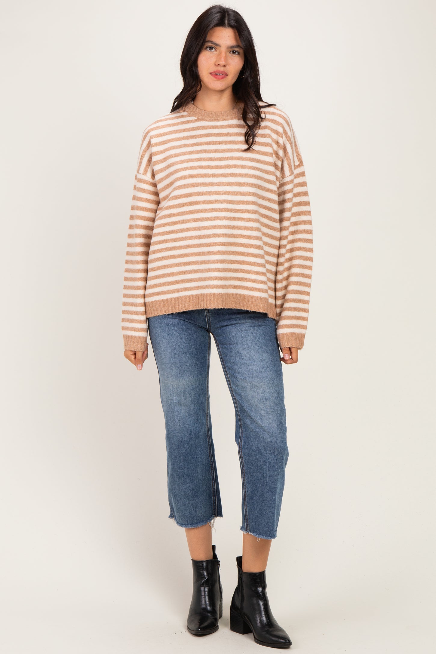 woman wearing a beige and white striped oversized sweater with blue cropped jeans and black ankle boots